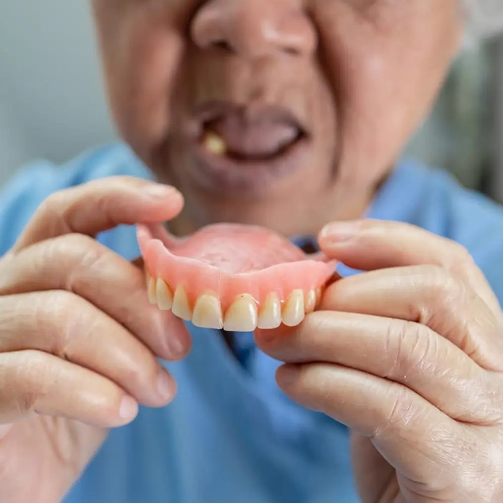 Persona mayor sosteniendo una prótesis dental removible (dentadura) antes de colocarla, mostrando necesidad de reemplazo | ECOS SALUD.